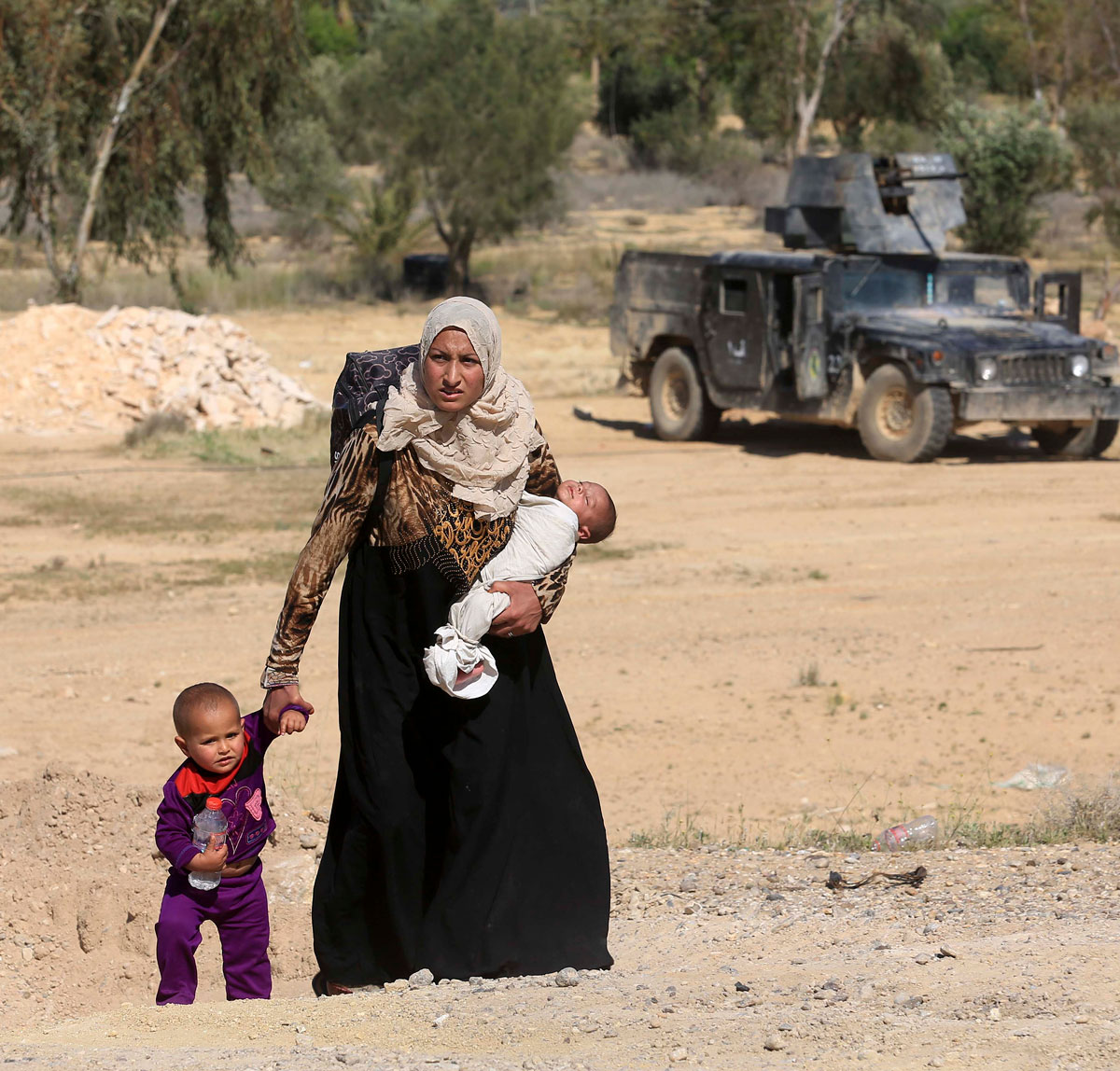 A mother flees fighting carrying baby and holding infant's hand