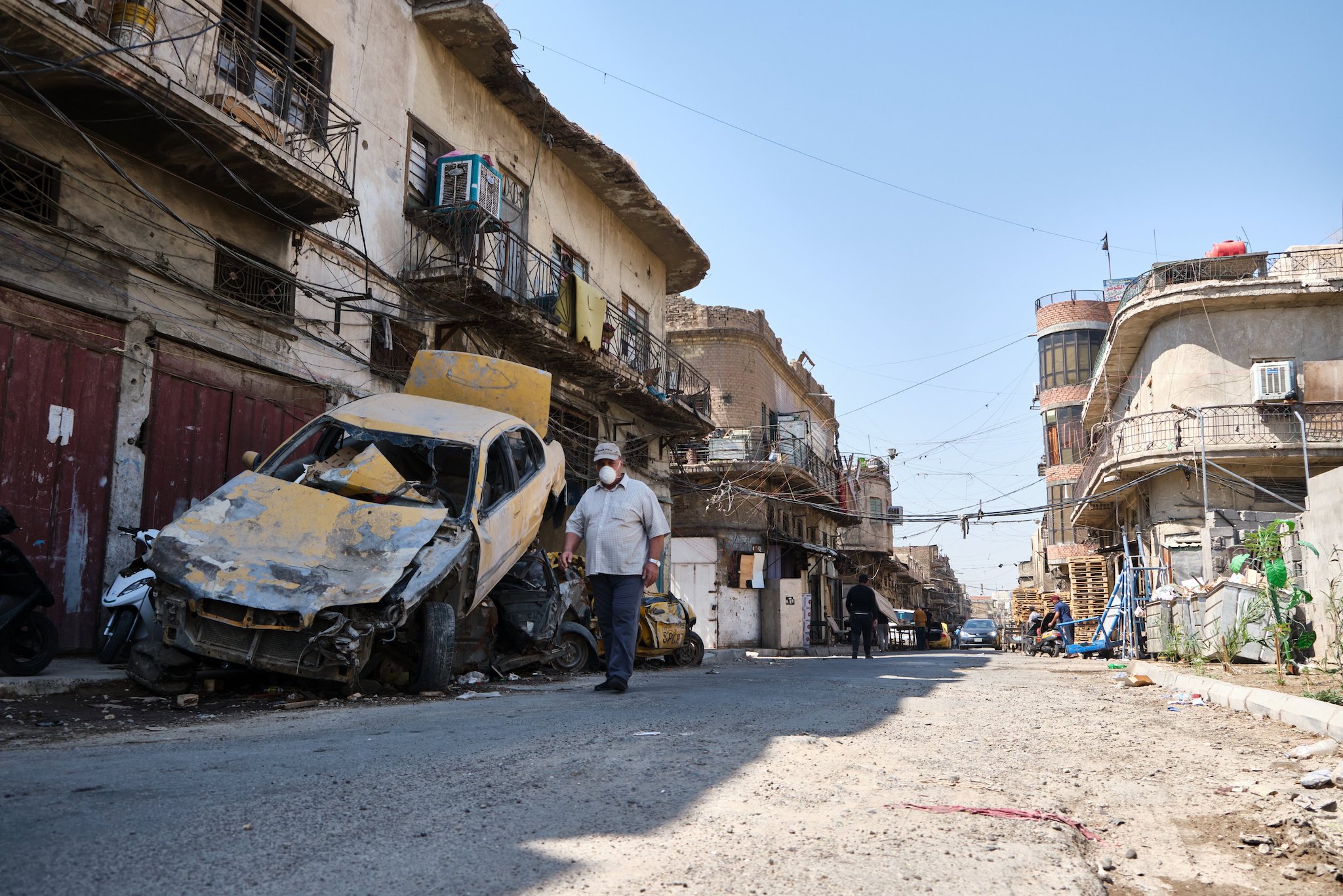 Man wearing protective mask walks past wrecked vehicles in the Iraqi capital Baghdad on July 6, 2020.